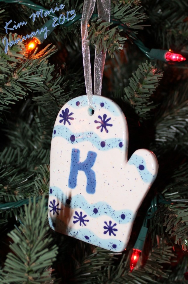 Ceramic Christmas tree ornament in the shap of a mitten with the letter K in the middle. Shades of blue iwth little snow flakes on the top and bottom.