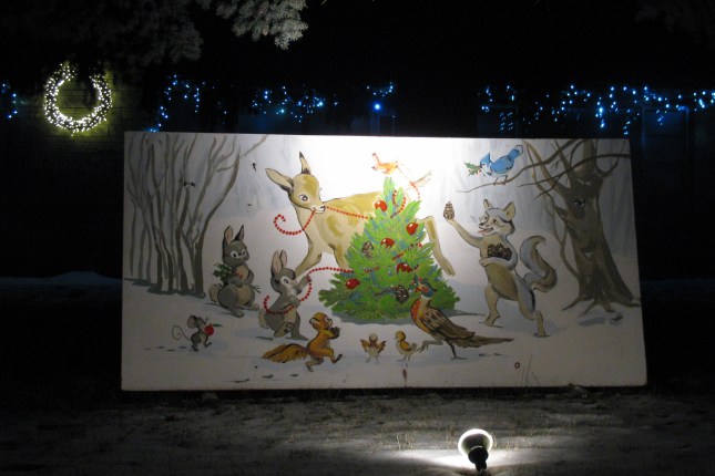 A card with forest animals decorating a pine tree in a meadow.