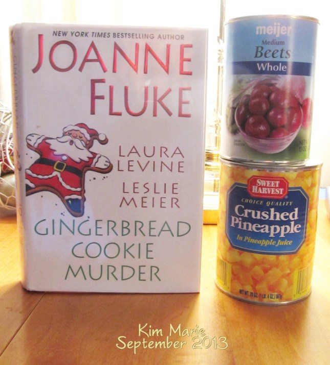 Image of Joanne Fluke's book shared with two other authors for short Christmas stories. Next to the book is a can of beets on top of a can of pineapple. 