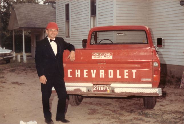 Dad by his old Chevrolet truck with a bumper sticker saying, Only Love Beats Milk