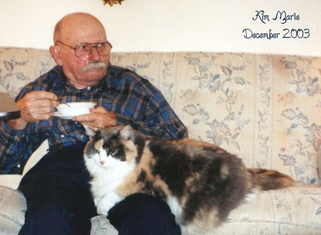 My dad at 79 sitting with his four-year old, long-haired, calico daisy kitty on his lap while he eats of bowl of cereal.