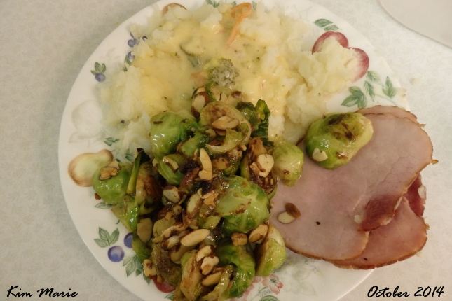 A dinner plate with the sprouts, ham, and mashed potatoes with cheese on them. Dinner is done, stick a fork in it!