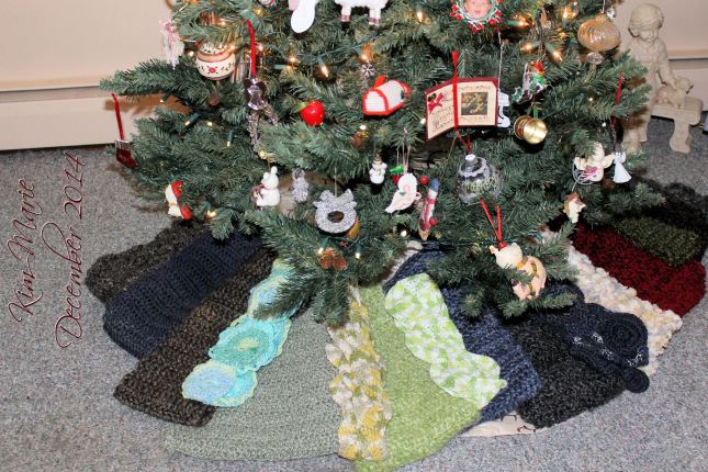 A Chrstmas Tree with numerous scraves of varying colors and width displayed beneath it. The tree is decorated for Christmas. 